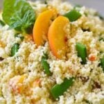 Couscous with Fresh Peaches & Sugar Snap Peas served in a white bowl, topped with fresh mint leaves and sliced peaches