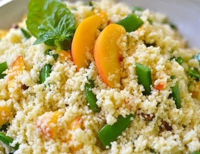Couscous with Fresh Peaches & Sugar Snap Peas served in a white bowl, topped with fresh mint leaves and sliced peaches
