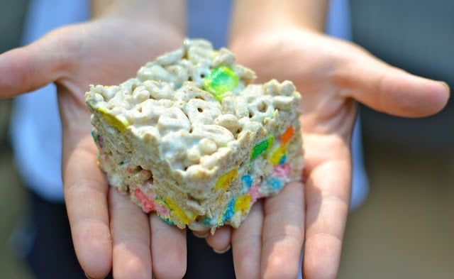 Child's hands holding a colorful Marshmallow Krispy Treats Used for Bribery square with rainbow sprinkles and cereal coating
