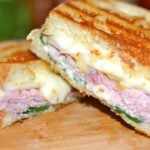 Ham & Cheese Panini with Pears & Spinach cut in half on wooden board, showing melted cheese, sliced ham, and green spinach between toasted b