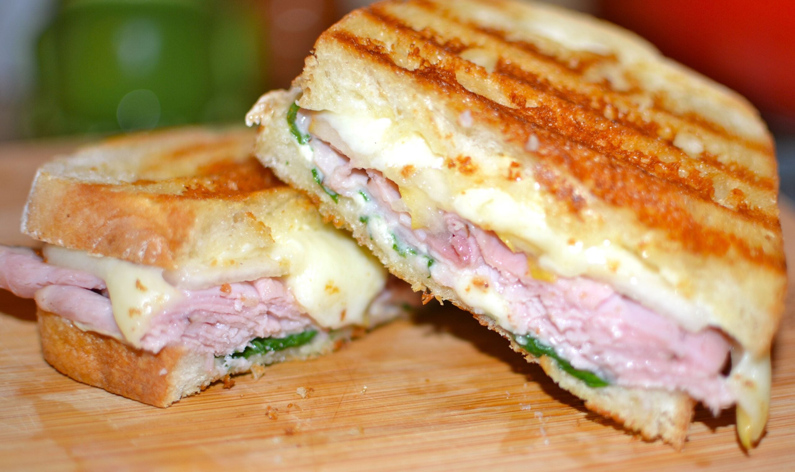 Ham & Cheese Panini with Pears & Spinach cut in half on wooden board, showing melted cheese, sliced ham, and green spinach between toasted b