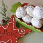 Powdered sugar-coated Mexican Wedding Cookies in a festive red and green container with holiday decorations and rosemary sprig