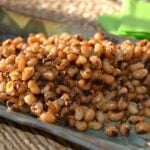 Crispy fried black eyed peas with charred edges piled on a blue plate with green napkin in background