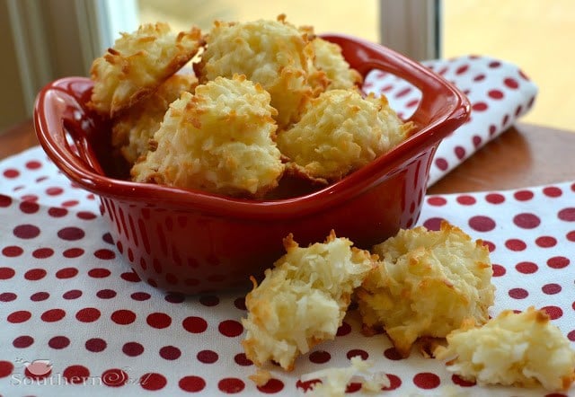 Golden coconut macaroons in red fish-shaped dish on red and white polka dot napkin with macaroons scattered on surface