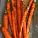 Roasted Carrots with Honey & Lemon arranged on a gray baking sheet with charred edges and green tops visible