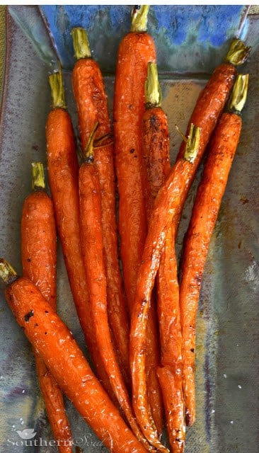 Roasted Carrots with Honey & Lemon arranged on a gray baking sheet with charred edges and green tops visible