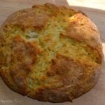 Freshly baked Irish Soda Bread with golden-brown crust on wooden surface, showing its characteristic round loaf shape and rustic texture