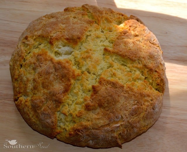 Freshly baked Irish Soda Bread with golden-brown crust on wooden surface, showing its characteristic round loaf shape and rustic texture