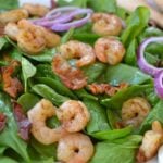 Spinach & Shrimp Salad with Warm Bacon Dressing topped with sautéed shrimp, crispy bacon, green peppers, and red onion rings