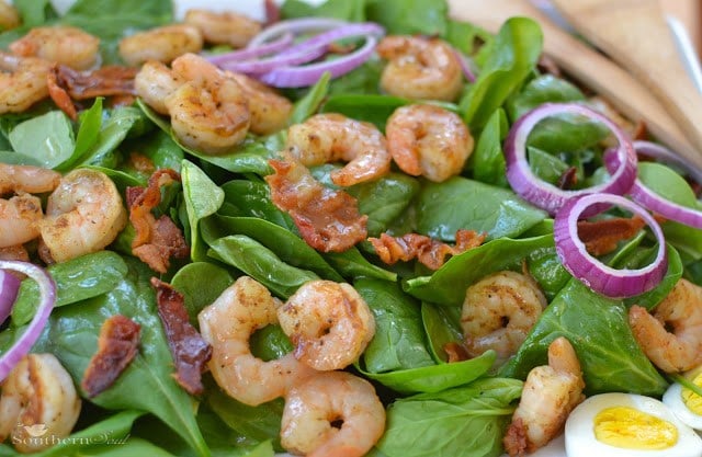 Spinach & Shrimp Salad with Warm Bacon Dressing topped with sautéed shrimp, crispy bacon, green peppers, and red onion rings