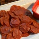 Crispy Pepperoni Chips with Dip served on a white plate with a red bowl of creamy dip beside it, overhead view