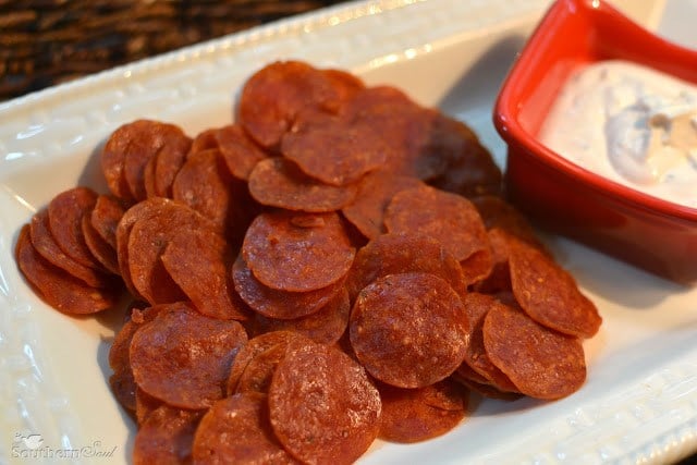 Crispy Pepperoni Chips with Dip served on a white plate with a red bowl of creamy dip beside it, overhead view