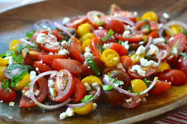 Heirloom Tomato Salad with sliced red tomatoes, yellow peppers, red onions, and crumbled feta cheese on a wooden plate