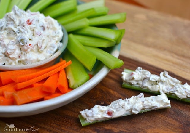 Cream Cheese and Olive from A Southern Soul Creamy, cool, and delicious Cream cheese and olive spread in a small bowl surrounded by carrots and celery, with two stuffed celery sticks sitting on the counter to the side.