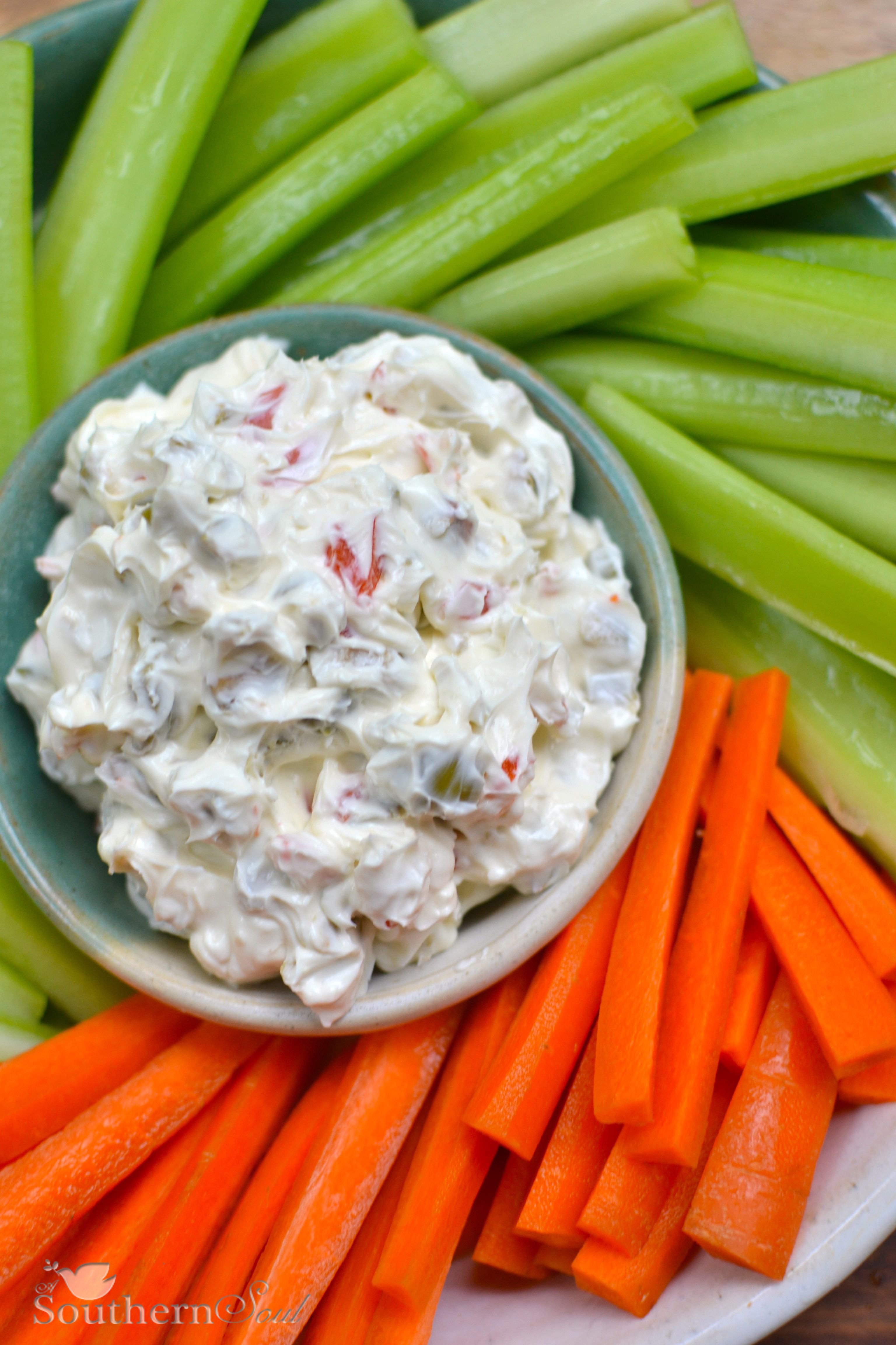 Creamy, cool, and delicious Cream cheese and olive spread in a small bowl surrounded by carrots and celery.