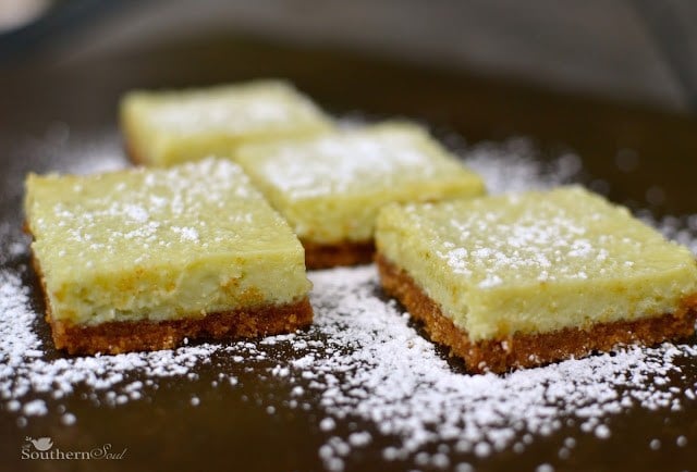 Lime bars dusted with powdered sugar on dark baking pan, showing buttery crust and creamy lime filling