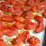 Halved red tomatoes roasted with olive oil and garlic on parchment paper, demonstrating how to roast and freeze tomatoes for Southern cookin