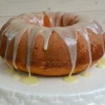 Easy Pumpkin Spice Dump Cake with white glaze drip and yellow sauce on white plate against wooden surface