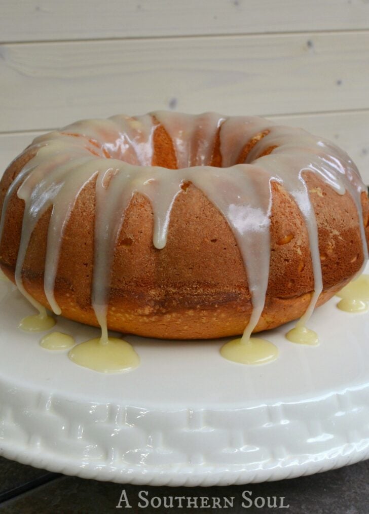Easy Pumpkin Spice Dump Cake with white glaze drip and yellow sauce on white plate against wooden surface