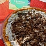 Thin Mints Ice Cream Pie with graham cracker crust, creamy filling, and crushed cookie topping in glass pie dish on red placemat