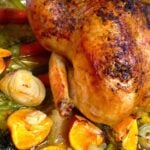 Roasted Chicken with Clementines, Garlic & Onions in a baking dish with golden-brown skin, surrounded by caramelized citrus, pearl onions, a