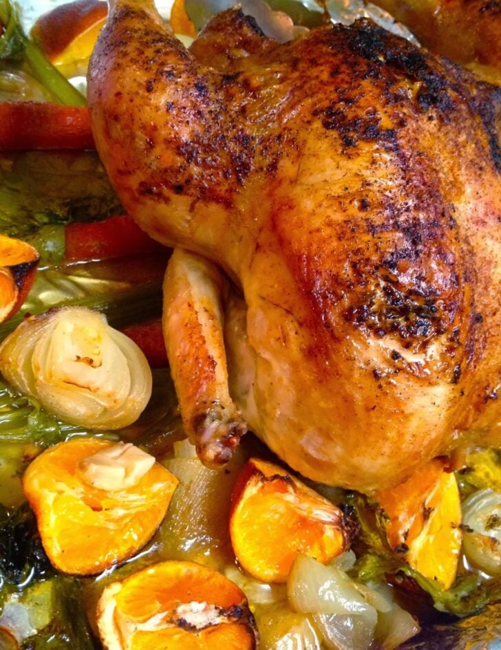 Roasted Chicken with Clementines, Garlic & Onions in a baking dish with golden-brown skin, surrounded by caramelized citrus, pearl onions, a