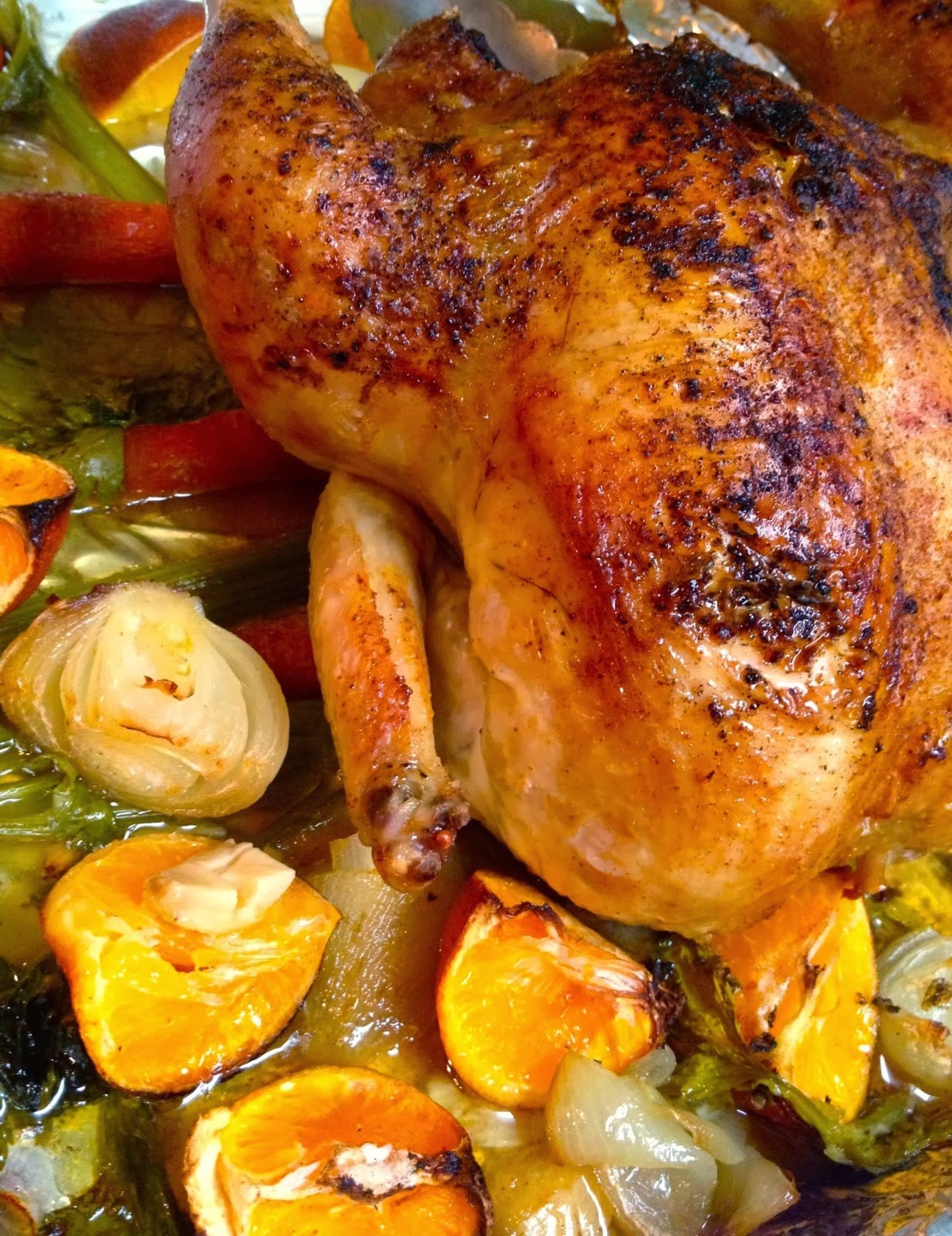 Roasted Chicken with Clementines, Garlic & Onions in a baking dish with golden-brown skin, surrounded by caramelized citrus, pearl onions, a