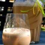 Homemade Bailey's Irish Cream in a wine glass with creamy foam head, large bottle behind with lime ribbon garnish