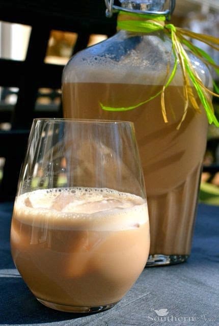 Homemade Bailey's Irish Cream in a wine glass with creamy foam head, large bottle behind with lime ribbon garnish
