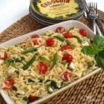 Orzo Pasta Salad with Fresh Vegetables & Feta served in white rectangular dish on woven placemat with fork and tin of Ardoguin in background