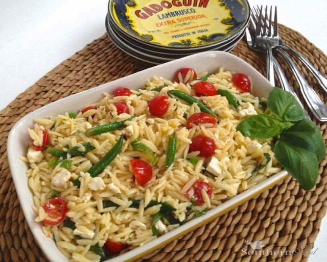 Orzo Pasta Salad with Fresh Vegetables & Feta served in white rectangular dish on woven placemat with fork and tin of Ardoguin in background