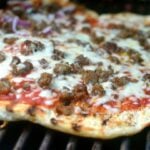 Grilled Pizza with ground beef, melted cheese, and red sauce on grill grates, viewed from above