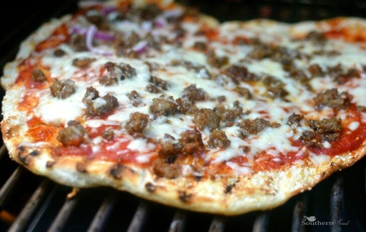 Grilled Pizza with ground beef, melted cheese, and red sauce on grill grates, viewed from above