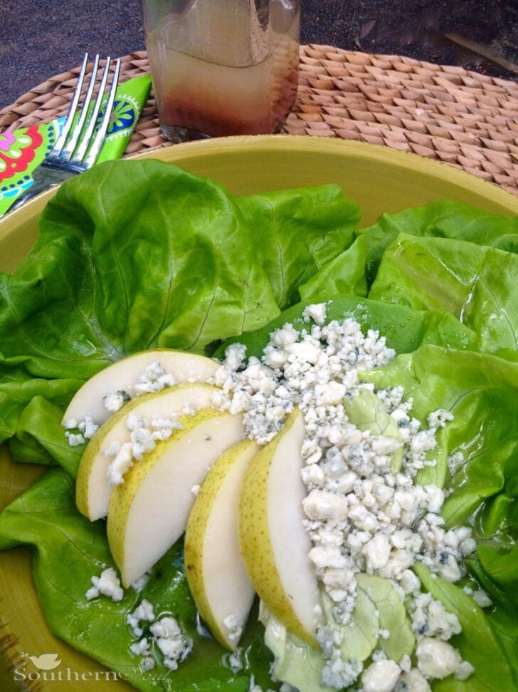 Pear & Blue Cheese Salad in yellow bowl with fresh lettuce, sliced pears, and crumbled blue cheese, fork and beverage visible