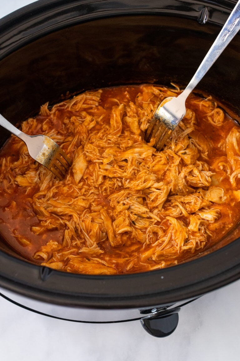 Shredded buffalo chicken in a slow cooker with two forks for serving, showing the 5-Ingredient Crock Pot Buffalo Chicken recipe result