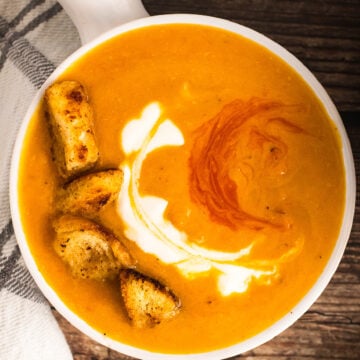 Roasted Sweet Potato Soup served in a white bowl with crispy croutons, cream swirl, and paprika garnish on dark wood
