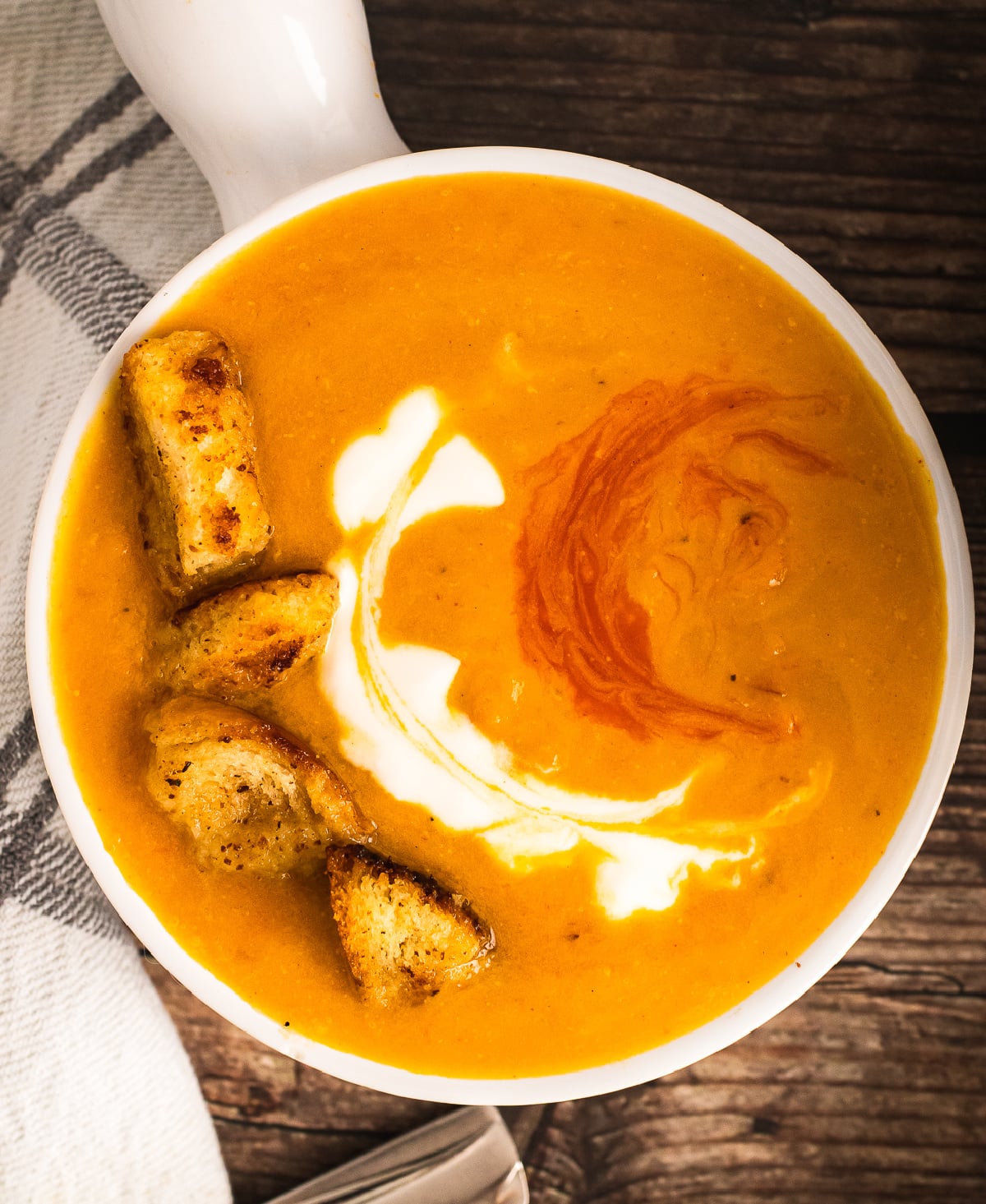 Roasted Sweet Potato Soup served in a white bowl with crispy croutons, cream swirl, and paprika garnish on dark wood