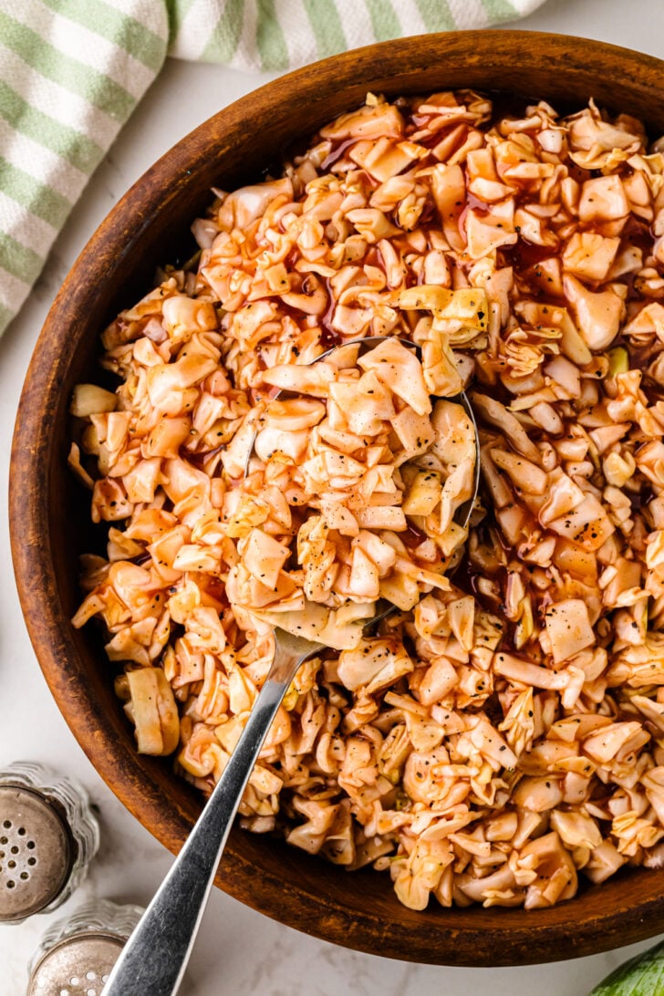 Carolina BBQ Red Slaw in wooden bowl with serving spoon and striped kitchen towel nearby