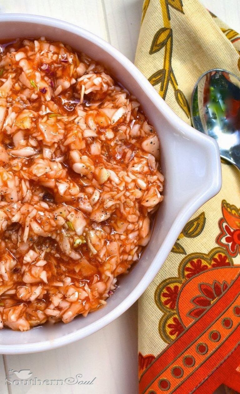 Carolina BBQ Red Slaw in white bowl with spoon, topped with black pepper on floral kitchen towel