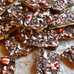 Chocolate Peppermint Bark broken into pieces on parchment paper, topped with crushed candy canes and white chocolate chips