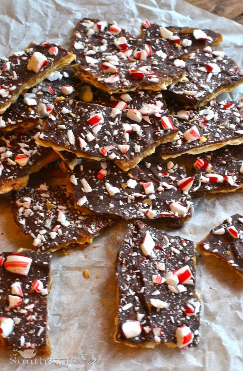 Chocolate Peppermint Bark broken into pieces on parchment paper, topped with crushed candy canes and white chocolate chips