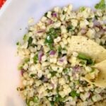 Grilled Corn Salsa in white bowl with corn kernels, diced red onion, cilantro, and lime crema drizzle on top