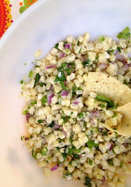 Grilled Corn Salsa in white bowl with corn kernels, diced red onion, cilantro, and lime crema drizzle on top