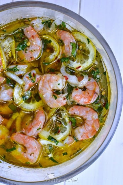 The Ultimate Southern Pickled Shrimp with lemon slices and fresh herbs in a white bowl viewed from above
