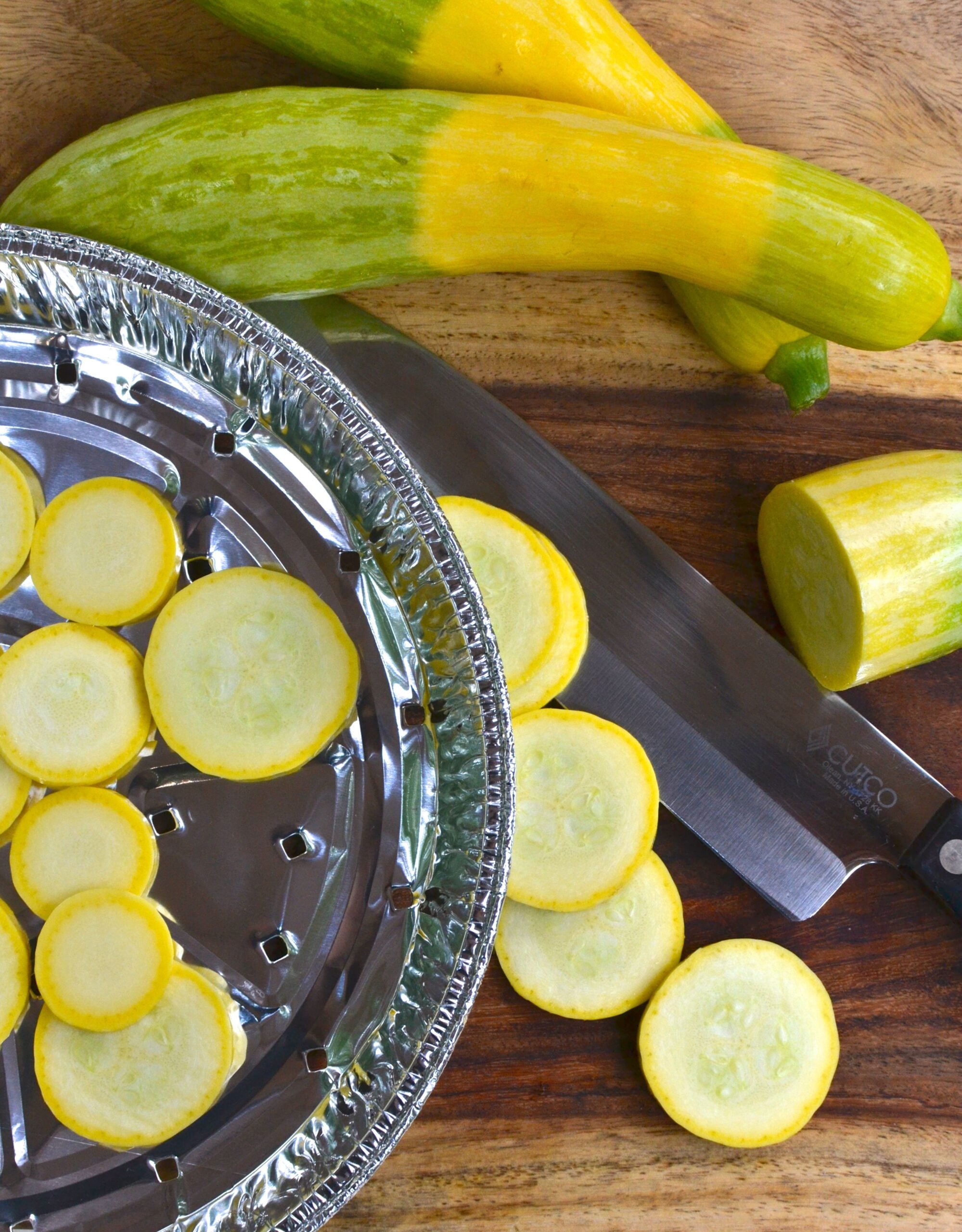 Sliced yellow squash on black disposable grill pan with whole squash and knife on wooden board. Hack: Grill Pan for .00
