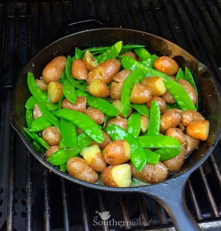 Grill Roasted Peas & Potatoes cooking in cast iron skillet on grates, showing browned potatoes and bright green pea pods