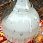 Easy Semi-Homemade Ranch Dressing in a glass pitcher with herbs and spices visible throughout the creamy white dressing