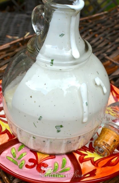 Easy Semi-Homemade Ranch Dressing in a glass pitcher with herbs and spices visible throughout the creamy white dressing