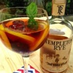 Father's Day Cocktail with Templeton Rye in coupe glass with citrus slices, cherries, fresh mint garnish, bottle beside on striped napkin