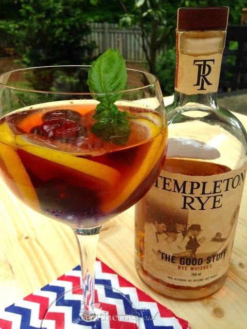 Father's Day Cocktail with Templeton Rye in coupe glass with citrus slices, cherries, fresh mint garnish, bottle beside on striped napkin